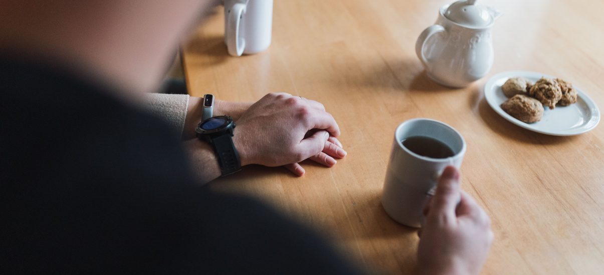 Van Oosterom parents hold hands at the kitchen table, tea and cookies are laid out.