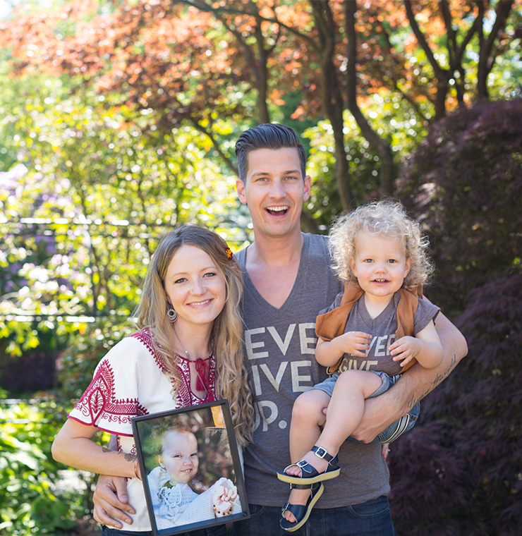 Canuck Place family smiling outdoors holding a photo frame of their child