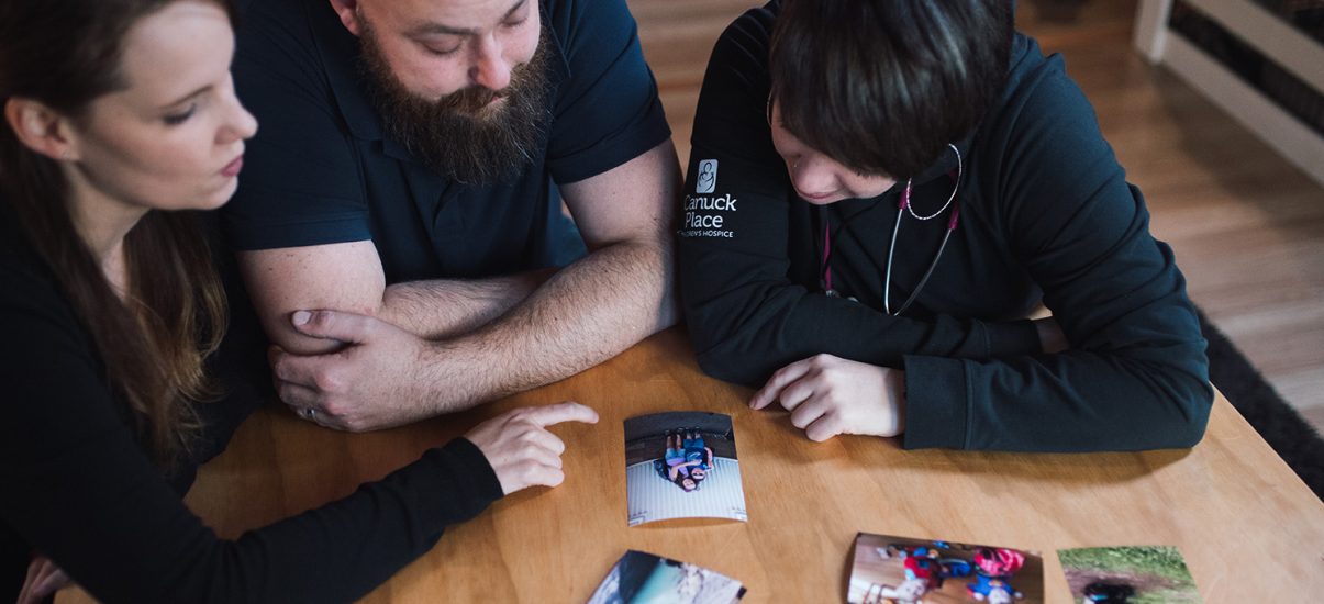 Father and mother with Canuck Place nurse practitioner looking at photos