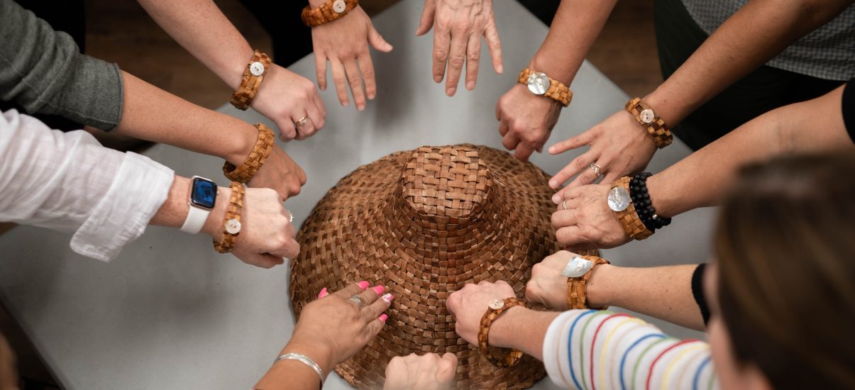 A group of arms wearing indigenous bracelets outstretched over an indigenous handmade hat