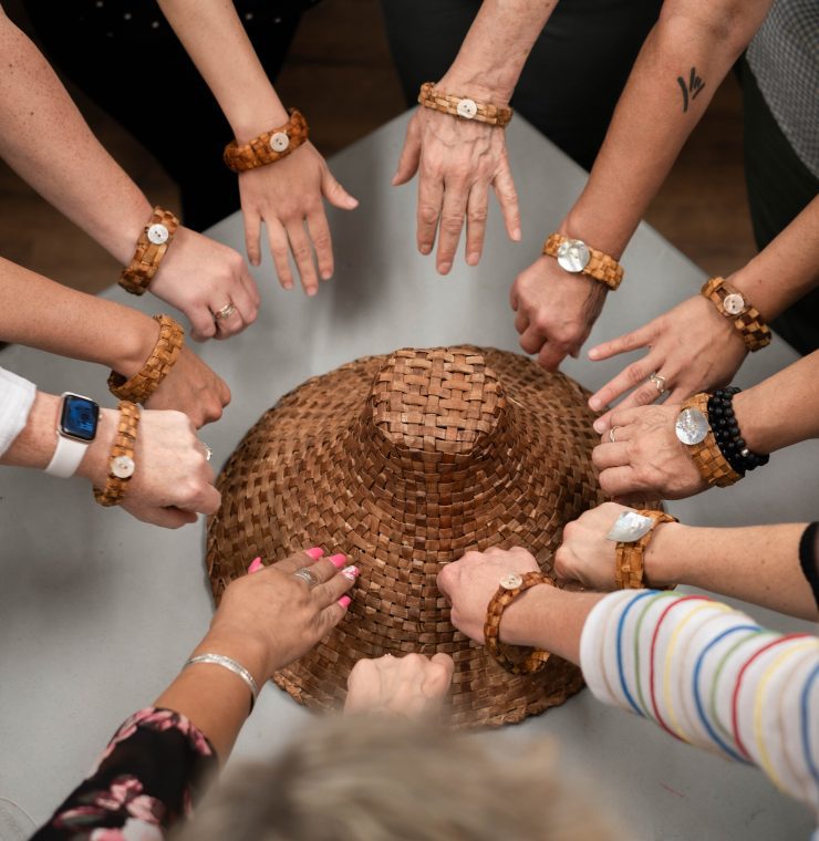 A group of arms wearing indigenous bracelets outstretched over an indigenous handmade hat