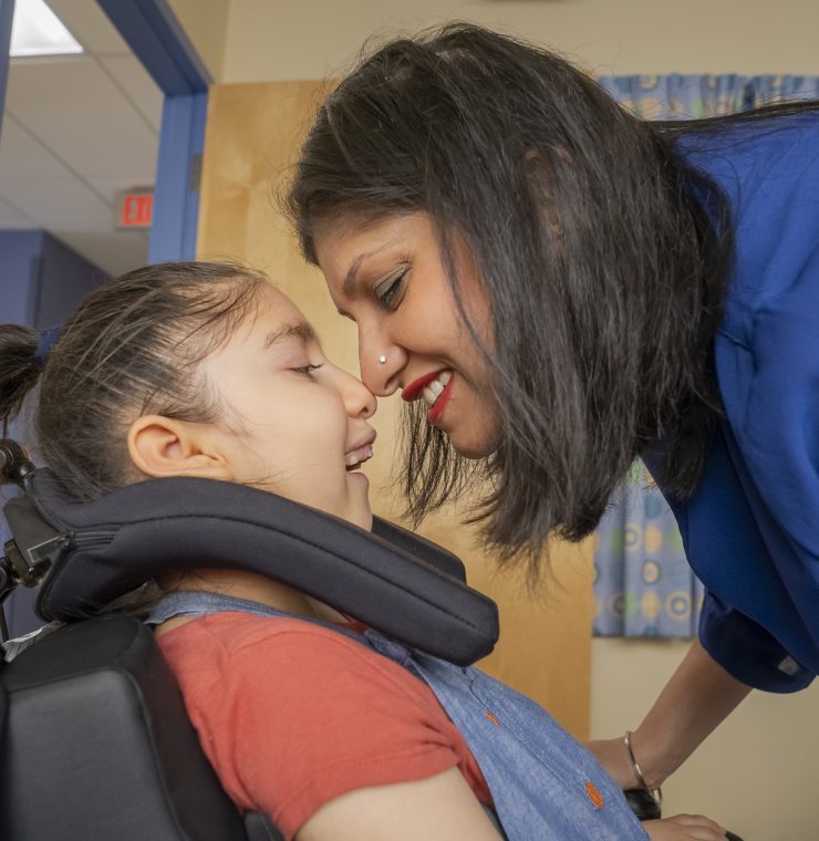A close-up of a child in a wheelchair with their mother leaning in and smiling