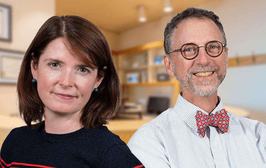 A portrait of a woman and a man smiling towards the camera. The office setting in the background is blurred. The woman has shoulder-length brown hair and wears a black sweater with thin red strips and small turquoise earrings, while the man sports a short beard, round glasses, and a colourful bow tie with a thin striped shirt.