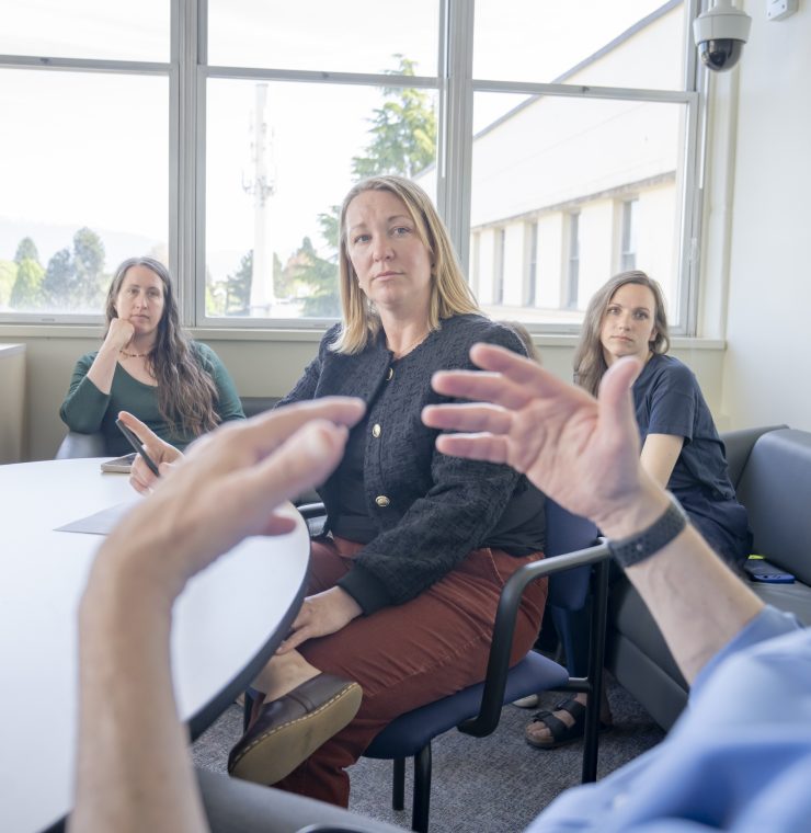 A group of adults sit in a circle in a sunlit room having a discussion
