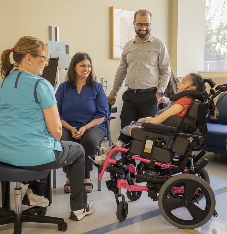 A healthcare provider speaks with a child in a wheelchair and their family