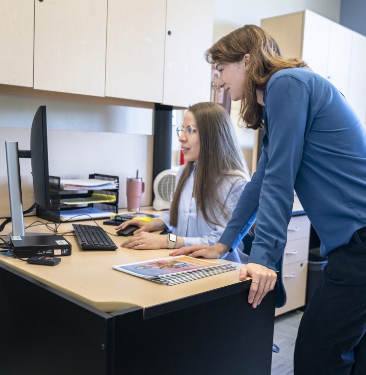 Two women huddle over a computer screen